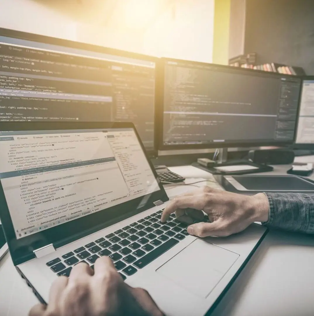 A person is using their laptop in front of multiple monitors.