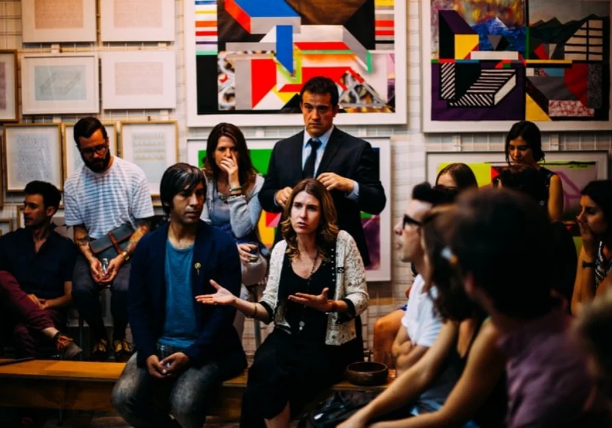 A group of people sitting around in front of some paintings.